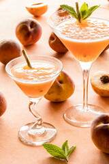 Two peach Bellinis surrounded by peaches and lit from behind.