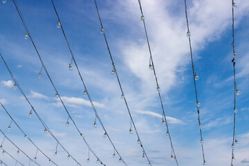 Wires with light bulbs on wires against cloudy blue sky background