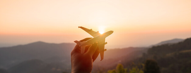 Hand holding a miniature airplane with the mountain view at sunrise, Summer vacation and travel concept