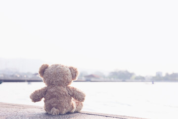 A sad teddy bear sits on a bridge alone looking at the sea in lonely with copy space. Toy, doll,...