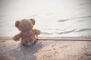 A sad teddy bear sits on a bridge alone looking at the sea in lonely with copy space. Toy, doll,...