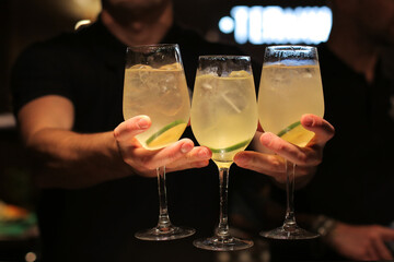 The waiter holds in his hand three alcoholic cocktails