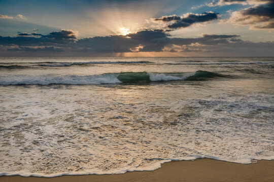 Rising sun shining through clouds above ocean