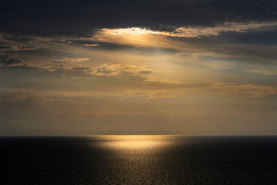 Sun shining through storm clouds and reflecting in ocean surface - Powered by Adobe