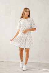 Girl in white dress at grey wall. Summer women's wardrobe.