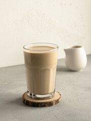 Coffee with milk on the wooden coaster, white pitcher, high key