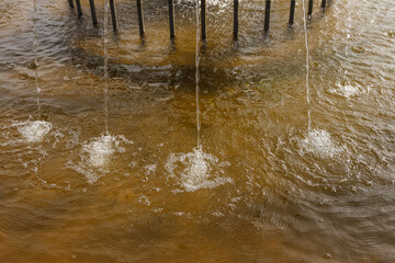 The surface of the water is perturbed by the fountain jets. Splashes on the water. Abstract background.
