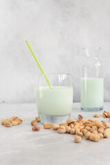 pistachio milk in a glass with a straw and in a bottle with pistachios on a grey background.