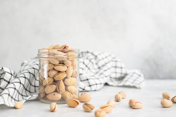 pistachios in a glass jar with a napkin on a gray background.
