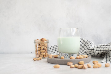 pistachio milk in a glass with pistachios on a grey plate and grey background.
