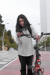 Fototapeta na wymiar Vertical image of a teenager consulting his smart phone holding a red bicycle in a city bike lane