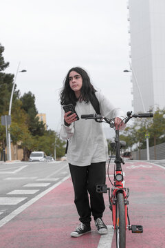 Vertical image of a teenager walking along a bike path pushing a bike while consulting his smart phone.