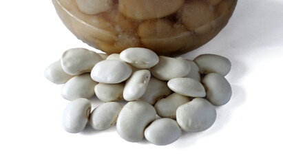 A handful of white beans next to a glass jar of canned beans . Isolated on a white background.