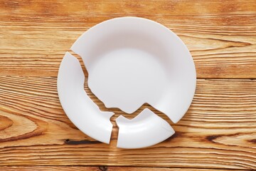 Top view on broken circle white plate on wooden background. The plate broke into three pieces....