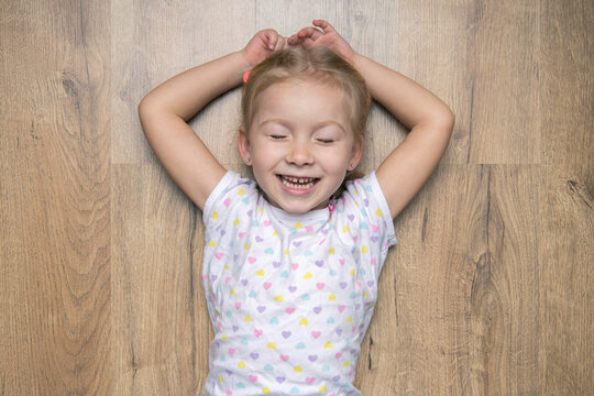 Smiling child girl with closed eyes lying on a wooden floor. Top view, flat lay.