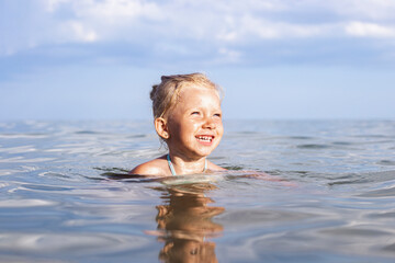 Cheerful smiling child blond girl swimming in the sea on a summer day.