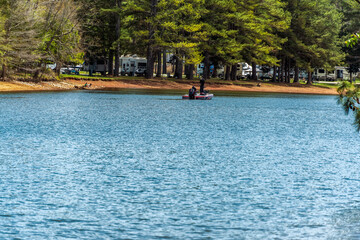 Man bass fishing in a bass boat, next to a RV campground, with two girls watching from shore, at Devils Step on Tim’s Ford Lake.