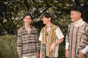 Three friends in boho style clothes having fun and bonding outdoors. Asian men being carefree and relaxed.