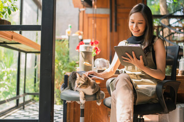 asian adult female creative designer casual relax working with her cat pet morning weekend at home studio,young asian asian wear apron research information for her workshop via tablet device - obrazy, fototapety, plakaty