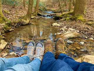 Guy and a girl sitting in a creek wearing hiking shoes and jeans in early spring after a long hike.