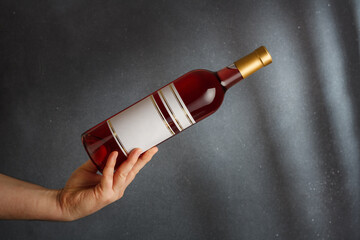 Male hand holding bottle of pink red wine, natural fruit alcohol liquor with empty label on grey background. Mock up, template for brand, copy space