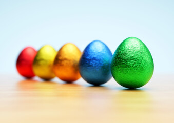 Chocolate easter eggs with shiny Red, yellow, orange, blue and green foil on white background. Close-up.	