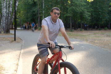 Obraz premium A man in dark glasses rides a bicycle in a public park in the summer. Sports and leisure