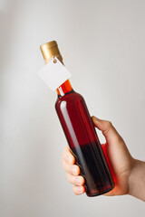 Male hand holds little bottle of red semisweet sweet or dry wine with no brand label, mockup template. Vertical shot, white background