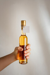 Hand holds small bottle of white dry, semisweet wine or sweet liquor with no brand label, mockup template. Vertical shot, white background