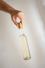 Hand holds small bottle of white dry, semisweet wine or sweet liquor with no brand label, mockup template. Vertical shot, white background