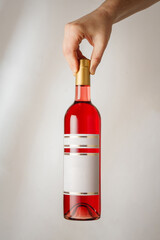 Male hand holds transparent bottle of red semisweet sweet or dry wine with no brand label, mockup template. Vertical shot, white background