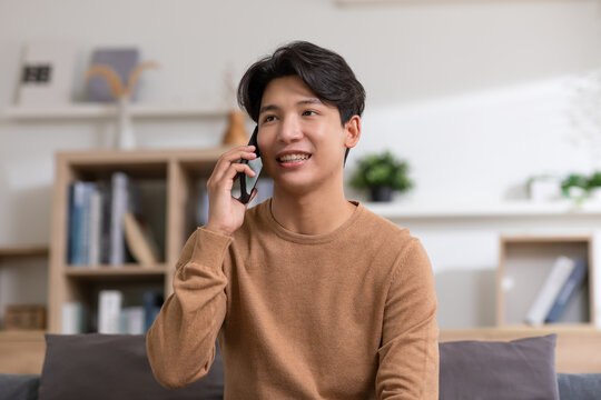 Happiness Handsome Asian Young Man Smiling Talking With Girlfriend On Mobile Phone At Home. Attractive Charming Teenager Holds Cellphone Talk With Someone.good Moment And Positive Mood. Candid Shot