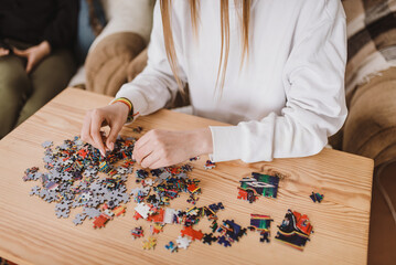 Young woman doing jigsaw puzzles close up. Hands and pieces of puzzles picture  laying in pile on the wooden table