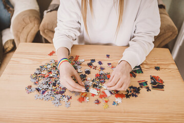 Young woman doing jigsaw puzzles close up. Hands and pieces of puzzles picture  laying in pile on...