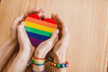 Lesbian couple holding a rainbow heart a symbol of lgbt. Female hands in rainbow bracelets and painted rainbow heart closeup