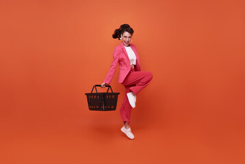 Smiling happy woman holding shopping basket and jumping isolated on orange background. - Powered by Adobe