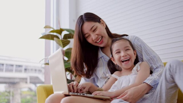 Daughter and mother sitting online studying from laptop smiling and happy in apartment living room. Toddler enjoy doing family writing activities. Caring for preschool learning. family lifestyle 
