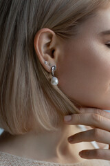 Luxurious woman with a short blond hairstyle and white pearl earrings, she is in profile with shiny...