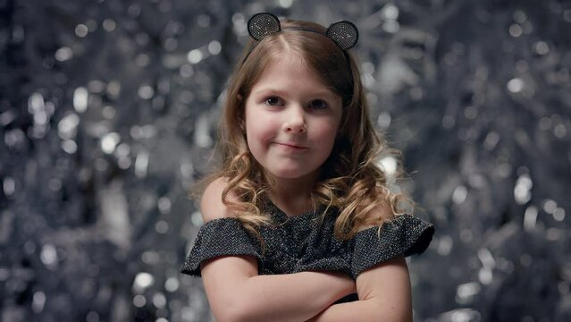 Funny Cheerful Little Girl Stands On Shiny Background. Celebration. She Put Her Hands On Her Chest.