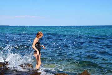 teenage girl in a black swimsuit in the splashes of sea waves
