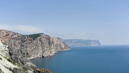 Aerial view of rocky coast and blue sea. Action. Flying above steep slopes of a mountain range, cliffs above calm water surface, summer nature landscape.