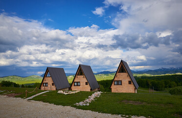 Fototapeta na wymiar Landscape with wooden cabins. A frame wooden houses in countryside with dramatic sky. A-frame wooden house on Durmitor mountain in Montenegro.