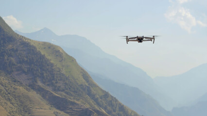 Fototapeta na wymiar Aerial view of a quadcopter flying above green mountains on morning haze background. Action. Drone filming video of natural landscape.