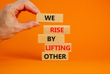 We rise by lifting other symbol. Concept words We rise by lifting other on wooden blocks. Businessman hand. Beautiful orange background. Business we rise by lifting other concept. Copy space.