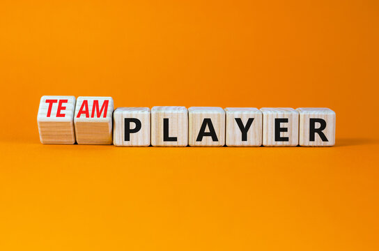 Player or teamplayer symbol. Turned wooden cubes and changed the concept word Player to Teamplayer. Beautiful orange table orange background, copy space. Business player or teamplayer concept.