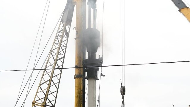 Close-up view of pile driver hammering concrete piles at a construction site. Overcast sky. Slow motion video. Deep foundation theme.