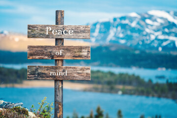 peace of mind text quote written on wooden signpost outdoors in nature with lake and mountain scenery in the background. Moody feeling.
