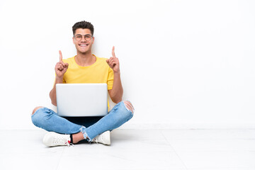 Young man sitting on the floor isolated on white background pointing up a great idea