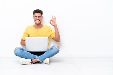 Young man sitting on the floor isolated on white background showing ok sign with fingers