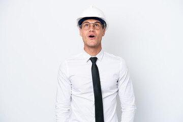 Young architect caucasian man with helmet and holding blueprints isolated on white background looking up and with surprised expression